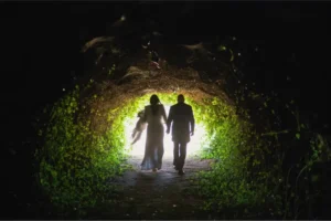 Novios caminando bajo un túnel de vegetación hacia la luz