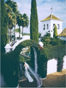 Bride walking under a whitewashed arch towards an Andalusian chapel