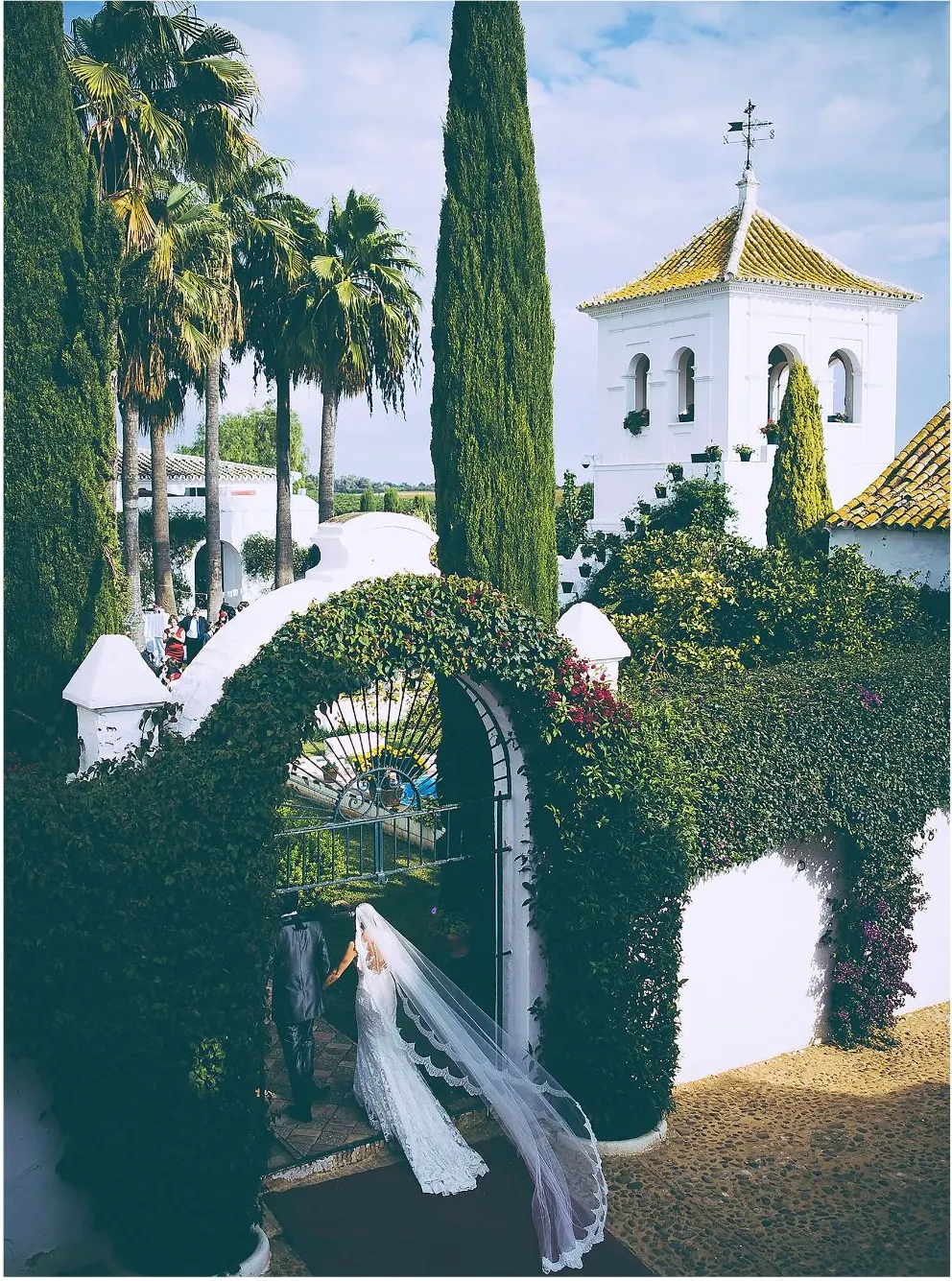 Bride walking under a whitewashed arch towards an Andalusian chapel