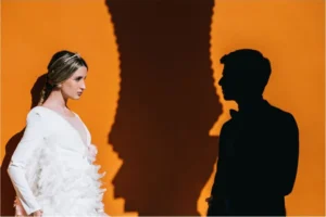 Pareja frente a una pared naranja con sus sombras, sesión de preboda
