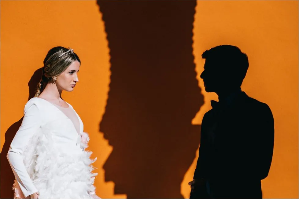 Pareja frente a una pared naranja con sus sombras, sesión de preboda
